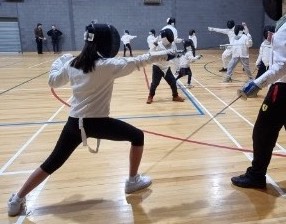 A girl of about 13 launching a fencing attack at her adult opponent